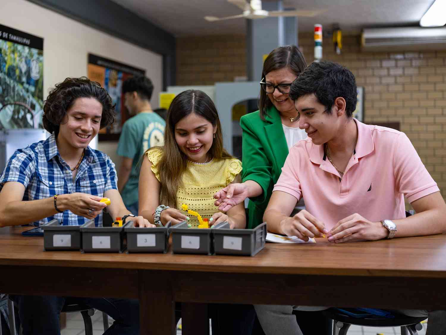 Tres estudiantes y una docente trabajan con piezas tipo LEGO en una actividad didáctica de aula.